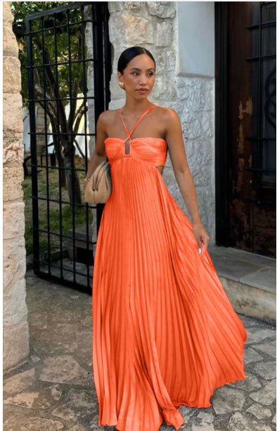 Woman in vibrant orange pleated maxi dress with halter neckline, standing by stone gate