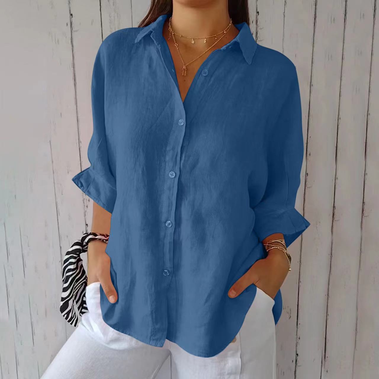 Blue button-down shirt with rolled sleeves, worn with white pants and layered necklaces